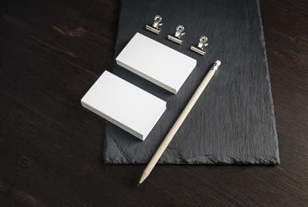 Two stacks of blank business cards, pencil and metal clamps on stone board background. Copy space.