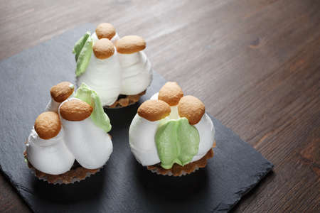Three cupcakes with sweet cream mushrooms on stone board. Selective focus.