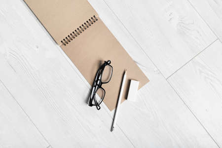 Blank kraft sketchbook, glasses, pencil and eraser on wooden background. Copy space. Flat lay.の写真素材