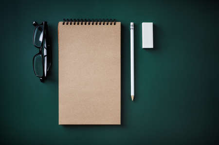 Blank kraft notebook, glasses, pencil and eraser on green background. Flat lay.の写真素材