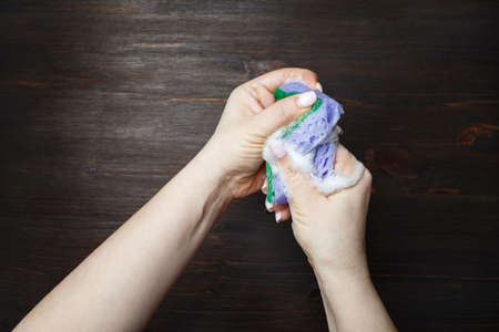 Woman hands and kitchen washing sponge with foam on wooden background.の写真素材