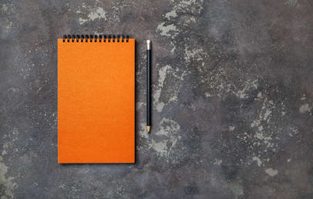 Photo of blank orange sketchbook and pencil on concrete background. Copy space for text. flat lay.の写真素材