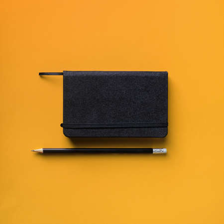 Photo of blank black notepad and pencil on yellow background. Responsive design template. flat lay.