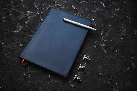 Blank blue notepad, pen and clips on black plaster background.の写真素材
