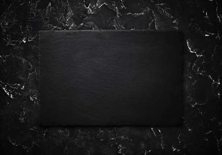 Photo of blank black stone slate plate on black plaster background. Top view with copy space. flat...