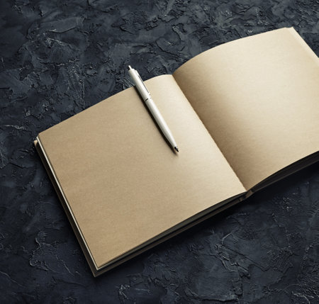 Photo of open kraft book with blank pages and pen on black plaster background.の写真素材