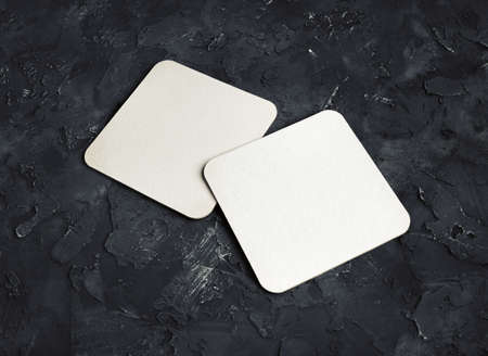 Blank white square beer coasters on black plaster background.の写真素材