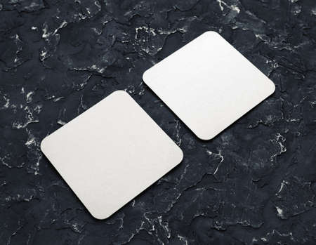 Two blank square beer coasters on black plaster background.の写真素材