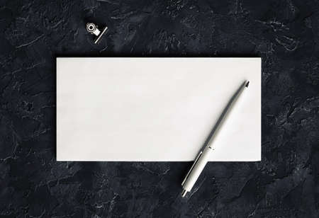 Blank envelope, pen and clip on black plaster background. Branding mockup. top view.の写真素材