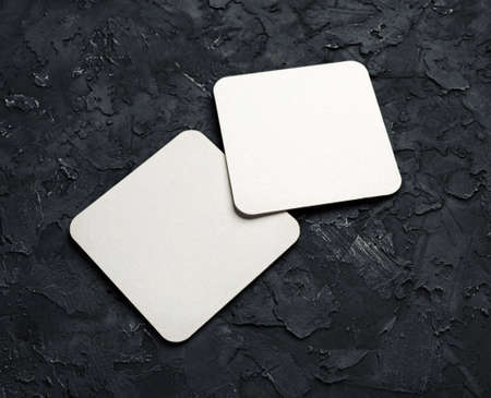 Two blank square beer coasters on black plaster background.の写真素材