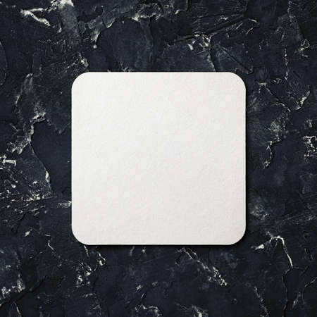 Blank white square beer coaster on black plaster background. top view.の写真素材