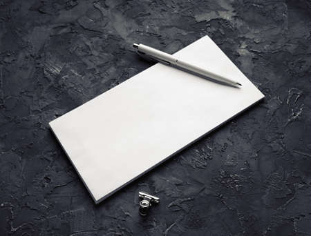 Photo of blank paper envelope, pen and metal clip on black plaster background.の写真素材