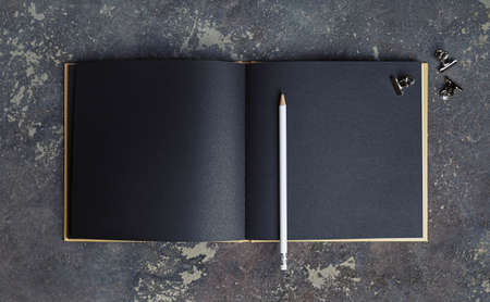 Blank black paper book, pencil and clips on concrete background. Responsive design template. top view.の写真素材