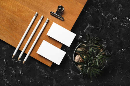 Branding identity mockup. Blank business cards, pencils, succulent plant, metal clip and wooden board on black plaster background. flat lay.の写真素材