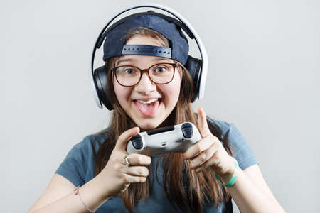 Happy teen girl in headphones and with a gamepad in his hands. Gamer girl playing video games.の写真素材