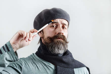 thoughtful bearded artist. Pensive man in beret with a brush in his hand looks at the camera.の写真素材