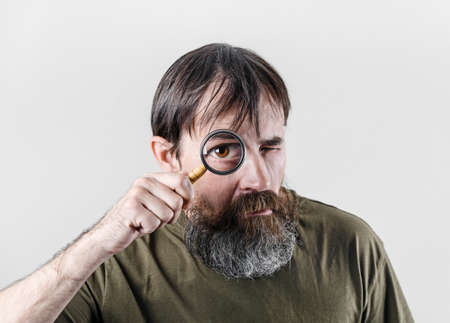 Bearded man looking through magnifying glass. Surprised male detective.の写真素材