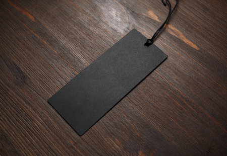 Blank black tag label with cord on wood table background. Mockup for branding identity.の写真素材