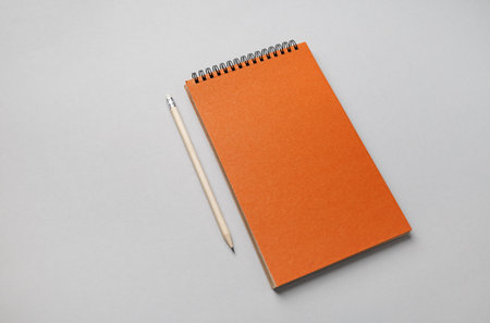 Photo of blank orange sketchbook and pencil on gray paper background.の写真素材