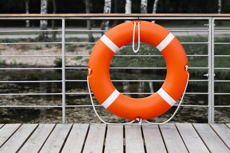 Orange lifebuoy hanging on the fence at the pier near the reservoir.
