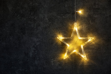 Decorated luminous Christmas Star LED light on black concrete texture background.