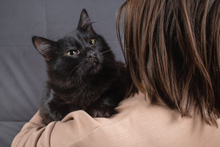 Black cat peeks out from behind a woman's shoulder.の写真素材