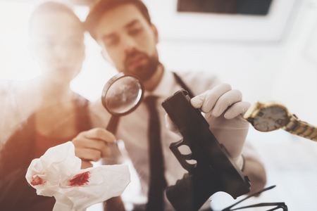 Private detective agency. Man with holster and woman are looking at gun with magnifying glass.の写真素材