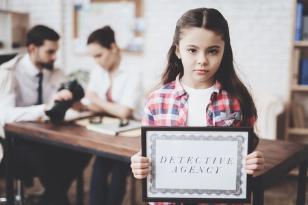 Private detective agency. Girl in shirt is posing with detective agency sign while man is showing clients photos on camera.の写真素材