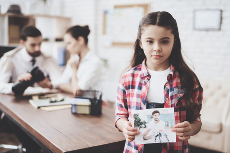 Private detective agency. Girl in shirt is posing with photo while man is showing clients photos on camera.の写真素材