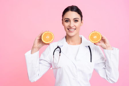 Portrait of smiling female doctor in white gown with stethoscope holding oranges isolated.の写真素材