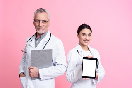 Portrait of smiling male and female doctors in white gowns with stethoscopes holding tablet and clipboard isolated.の写真素材