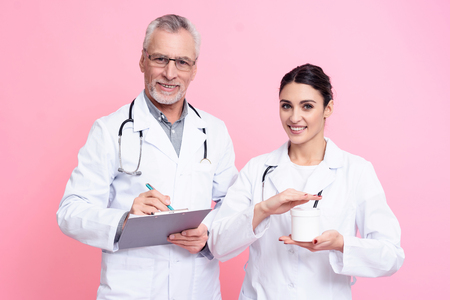 Portrait of smiling male and female doctors in white gowns with stethoscopes holding clipboard and white box isolated.の写真素材