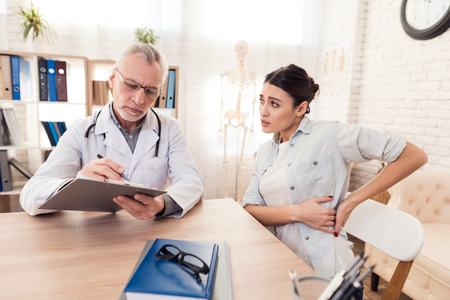 Doctor in white gown with stethoscope and female patient in office. Patient's side hurts.の写真素材