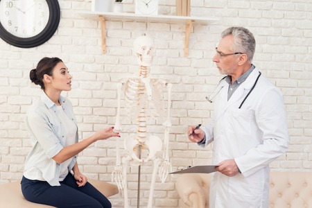 Doctor in white gown with stethoscope and female patient in office. Woman is telling symptoms.の写真素材