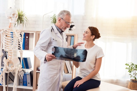 Doctor in white gown with stethoscope and female patient in office. Doctor is showing x-ray of hips.の写真素材
