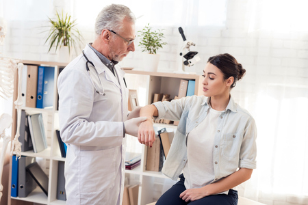 Doctor in white gown with stethoscope and female patient in office. Doctor is examining woman's arm.の写真素材
