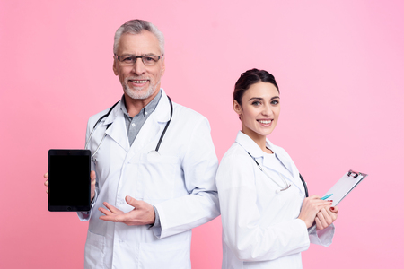 Portrait of smiling male and female doctors in white gowns with stethoscopes holding tablet and clipboard isolated.の写真素材