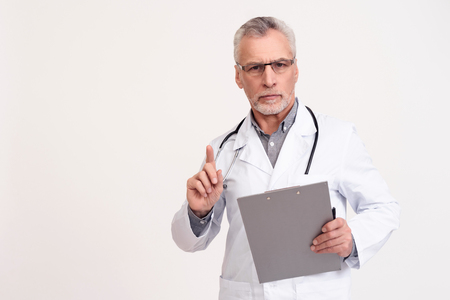 Portrait of serious doctor in white gown with stethoscope and clipboard isolated.の写真素材