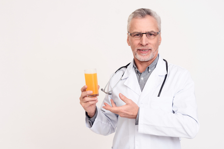 Portrait of doctor in white gown with stethoscope holding glass of juice isolated.の写真素材