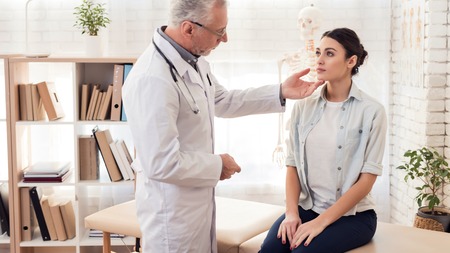 Doctor in white gown with stethoscope and female patient in office. Doctor is examining woman.の写真素材