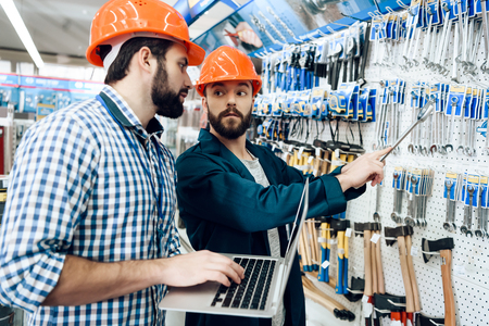 Two salesmen in construction helmets are checking equipment selection in power tools store.