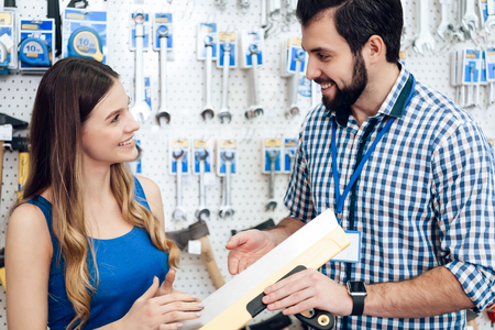 Salesman in checkered store is showing female client putty spatula in power tools store.の写真素材