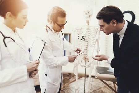 Physiotherapist showing anatomical model of spine to patient in medical office.