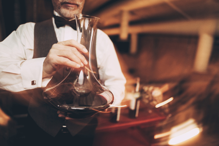 Close up. Sommelier with bow tie agitates wine in decanter. Wine tasting. Blurred. Professional degustation expert in winemaking.の写真素材