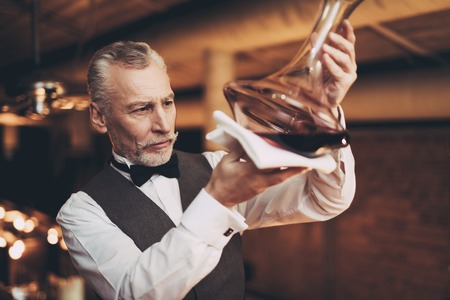 Experienced elegant sommelier looks at wine sediment in decanter. Wine degustation. Male skilled sommelier estimates alcoholic drink.の写真素材