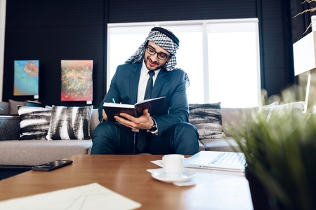 Bearded arab businessman in suit taking notes on couch at office room.