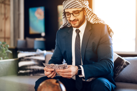 Bearded arab businessman in suit counting money on couch at hotel room.の写真素材