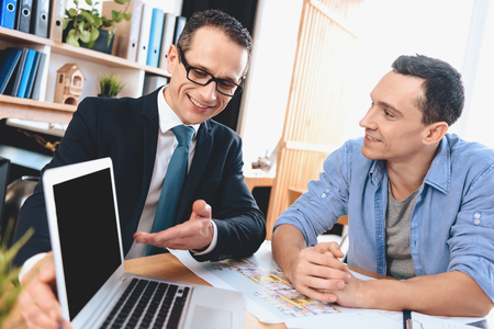 Realtor in suit sitting at desk in office. Realtor is presenting laptop to father, mother and son.の写真素材