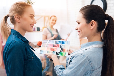 Three girls at garment factory. They are looking at colors for new dress on pattern. They are happy and fashionable.の写真素材