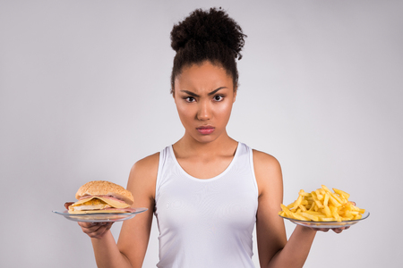 Black girl holding cheeseburger and fries isolated on white background.の写真素材